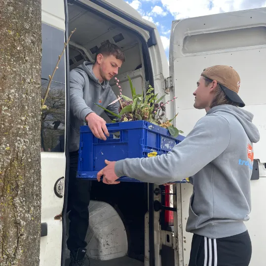 Twee verhuizers tillen een blauwe container uit een vrachtwagen tijdens een professionele verhuizing bij een woning.