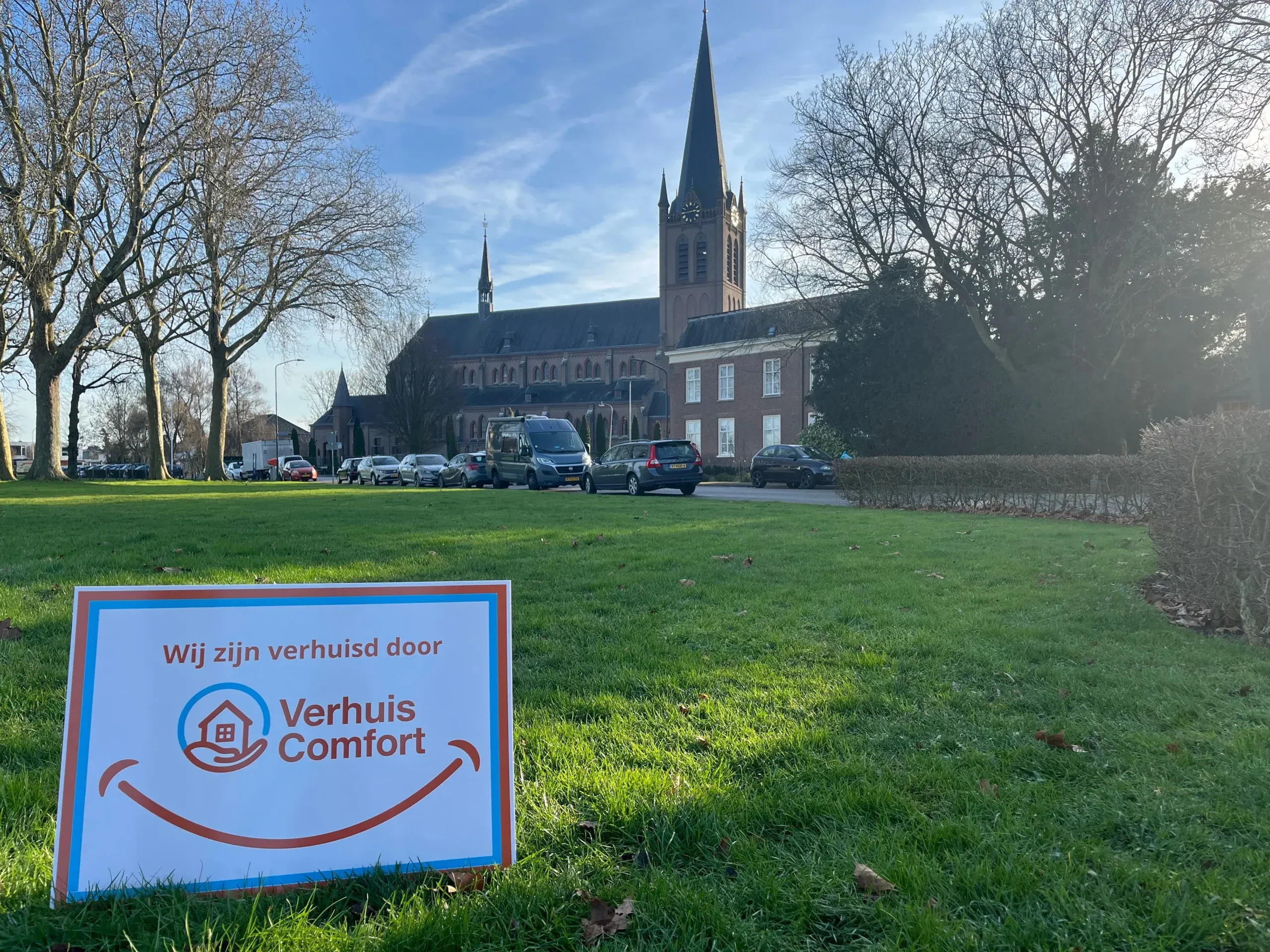 Verhuis Comfort-bord langs een straat met de kerk van Beuningen op de achtergrond.